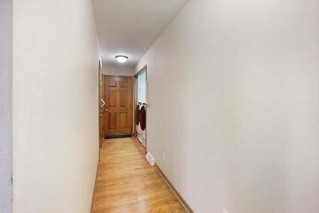 corridor with washer and dryer, light wood-style flooring, and baseboards