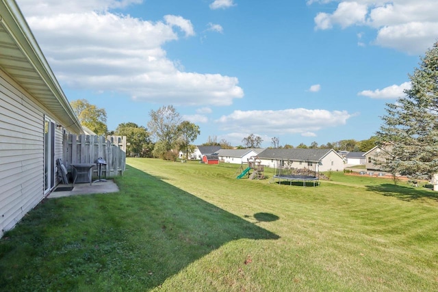 view of yard with a trampoline, a playground, and fence