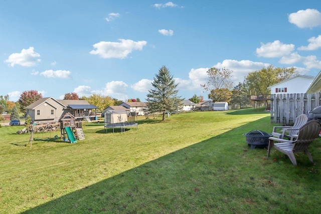 view of yard featuring a trampoline, a playground, and a fire pit