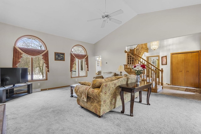 carpeted living room featuring high vaulted ceiling, baseboards, stairway, and ceiling fan with notable chandelier