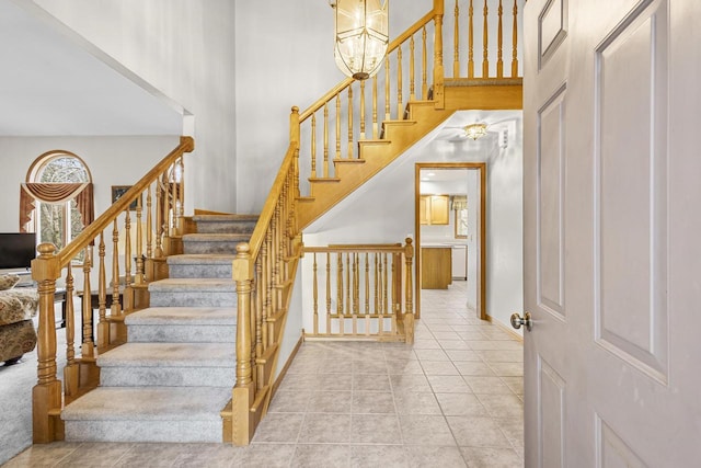 staircase with a towering ceiling, baseboards, a notable chandelier, and tile patterned floors