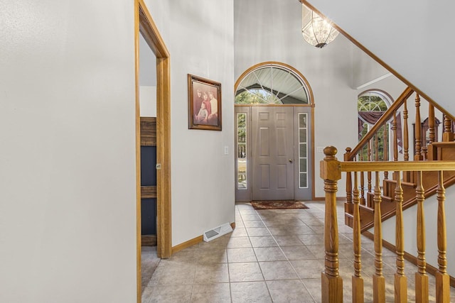 entrance foyer with visible vents, baseboards, stairs, a towering ceiling, and tile patterned floors