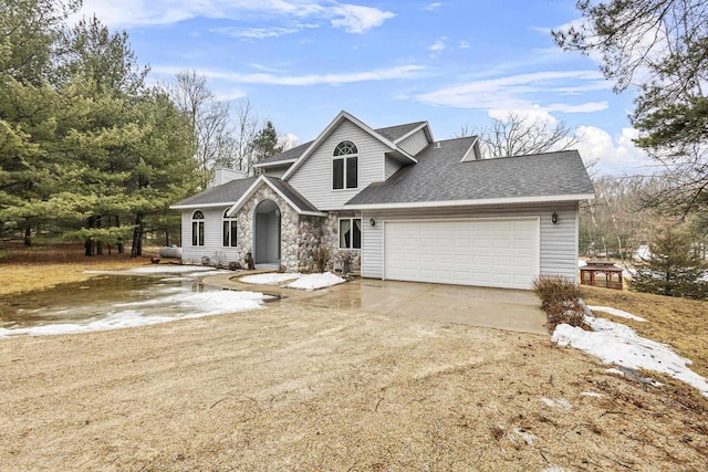 traditional-style house featuring a garage, a shingled roof, concrete driveway, stone siding, and a chimney