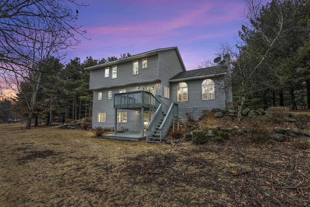 back of house at dusk with stairs, a chimney, and a wooden deck