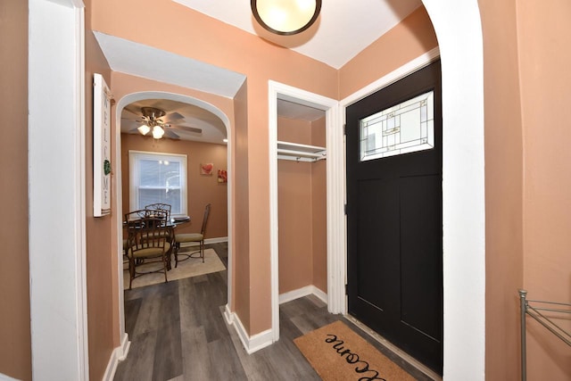 entryway with arched walkways, a ceiling fan, baseboards, dark wood-style floors, and plenty of natural light