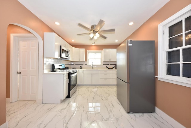 kitchen featuring decorative backsplash, marble finish floor, stainless steel appliances, white cabinetry, and a sink