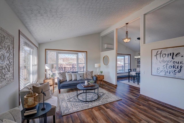 living area featuring vaulted ceiling with beams, baseboards, a wall unit AC, wood finished floors, and a textured ceiling