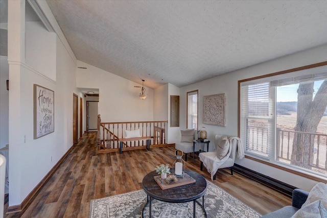 living area featuring wood finished floors, baseboards, vaulted ceiling, a textured ceiling, and an upstairs landing