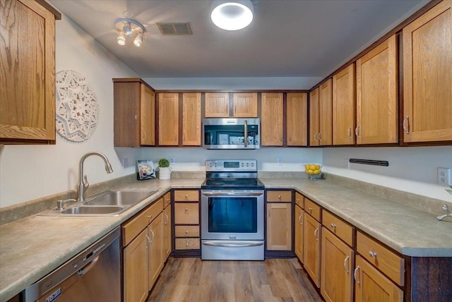 kitchen with visible vents, dark wood-type flooring, brown cabinetry, stainless steel appliances, and a sink