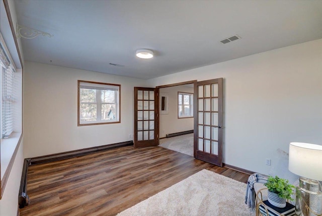 unfurnished room with baseboard heating, french doors, visible vents, and wood finished floors