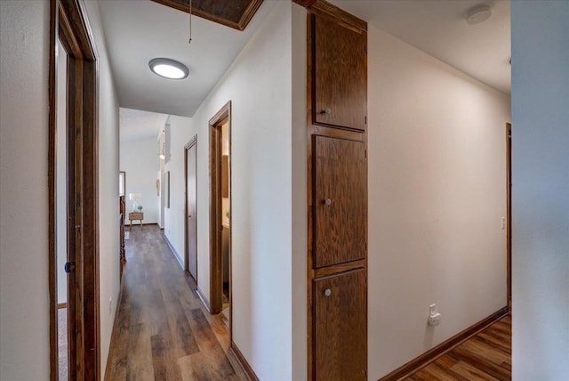 corridor featuring baseboards, attic access, and wood finished floors