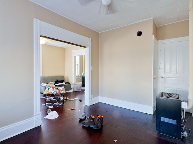 interior space with baseboards, wood finished floors, a ceiling fan, and heating unit