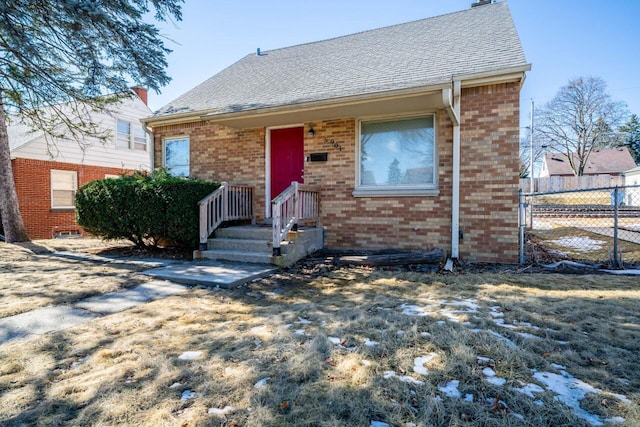 view of front of home featuring a shingled roof, fence, and brick siding