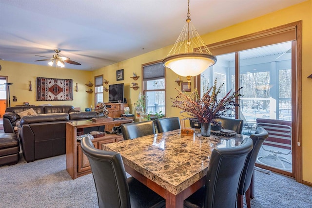 dining space with a ceiling fan and light colored carpet