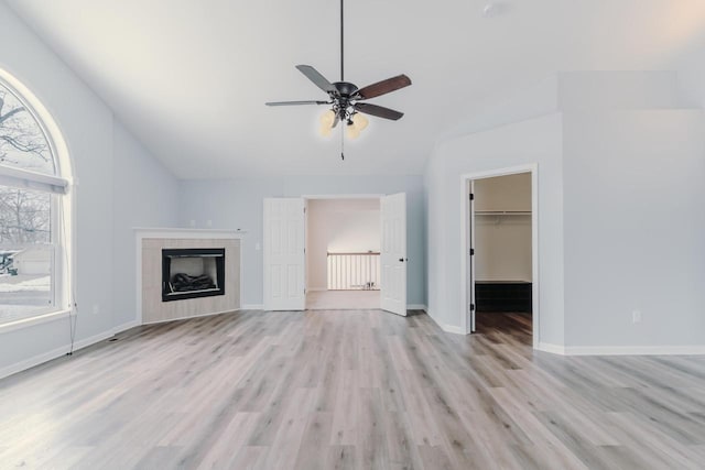 unfurnished living room with lofted ceiling, light wood-type flooring, baseboards, and a tile fireplace