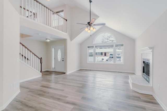 unfurnished living room featuring stairs, high vaulted ceiling, a tiled fireplace, and wood finished floors