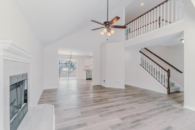 unfurnished living room featuring light wood-type flooring, high vaulted ceiling, stairway, and a tile fireplace