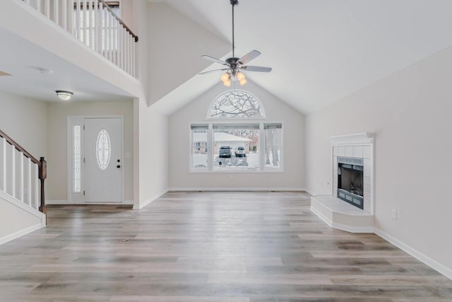 foyer entrance featuring stairs, a fireplace, high vaulted ceiling, and wood finished floors