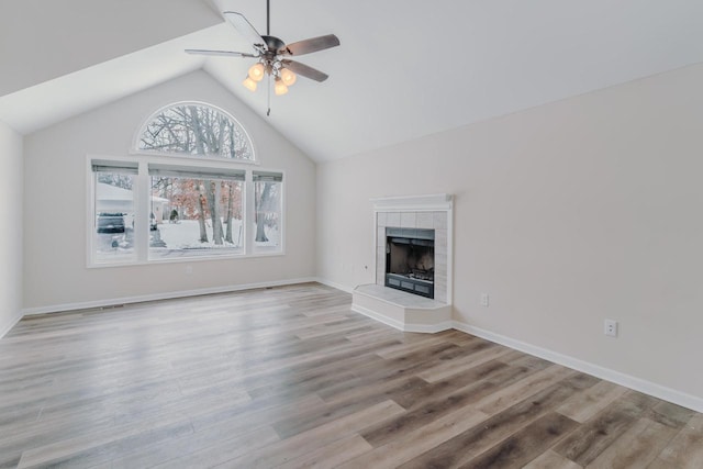 unfurnished living room with ceiling fan, a tiled fireplace, wood finished floors, and lofted ceiling