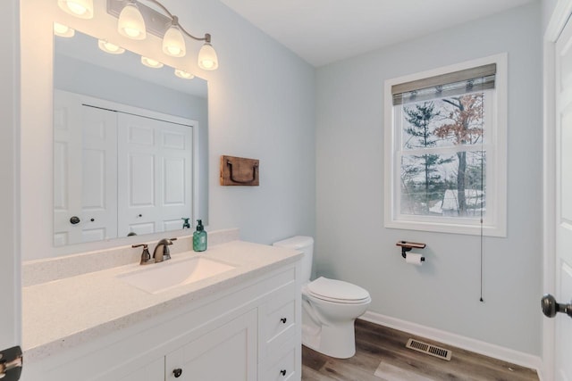 bathroom with toilet, wood finished floors, vanity, visible vents, and baseboards