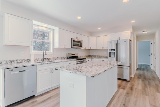 kitchen featuring appliances with stainless steel finishes, light wood-type flooring, white cabinetry, and a sink