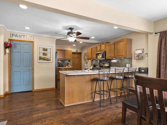 kitchen featuring dark wood-style floors, brown cabinets, a peninsula, stainless steel appliances, and a sink