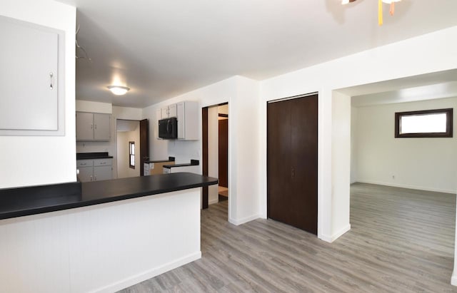 kitchen with light wood finished floors, dark countertops, gray cabinetry, black microwave, and baseboards