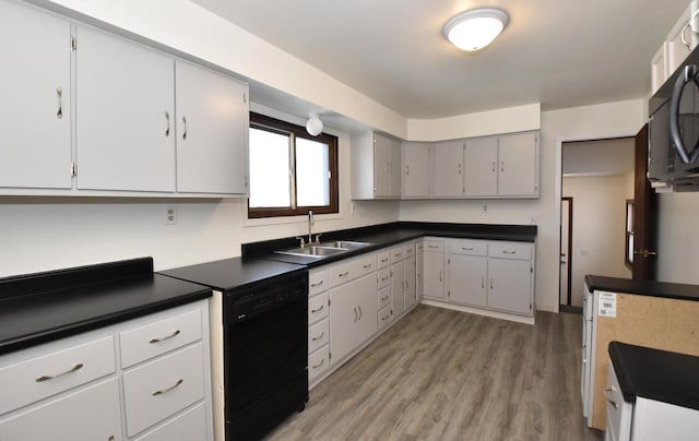 kitchen with dark countertops, black appliances, light wood finished floors, and a sink