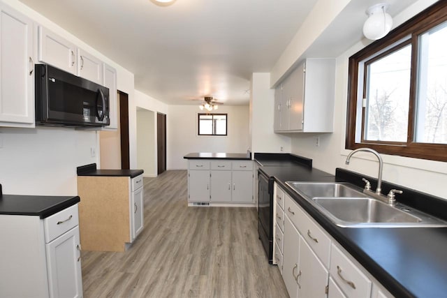 kitchen featuring dishwashing machine, dark countertops, a sink, and light wood-style floors