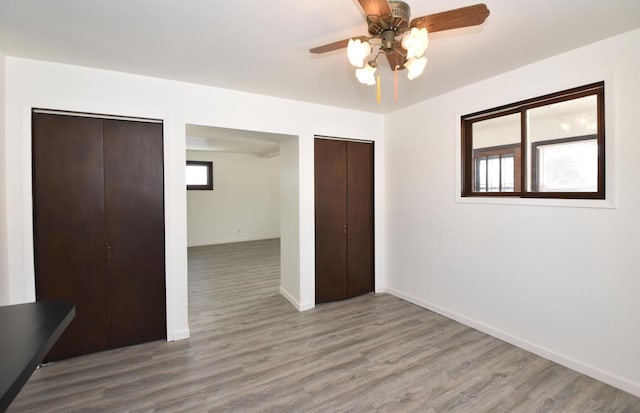 unfurnished bedroom with light wood-type flooring, two closets, a ceiling fan, and baseboards