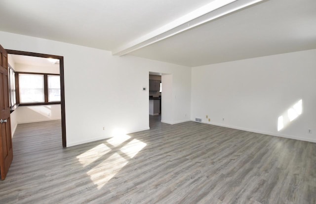 spare room featuring beamed ceiling, baseboards, and wood finished floors