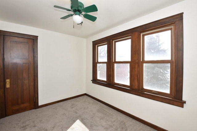 spare room featuring light carpet, a ceiling fan, and baseboards