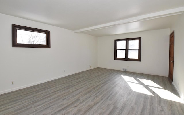 spare room with beam ceiling, visible vents, baseboards, and wood finished floors