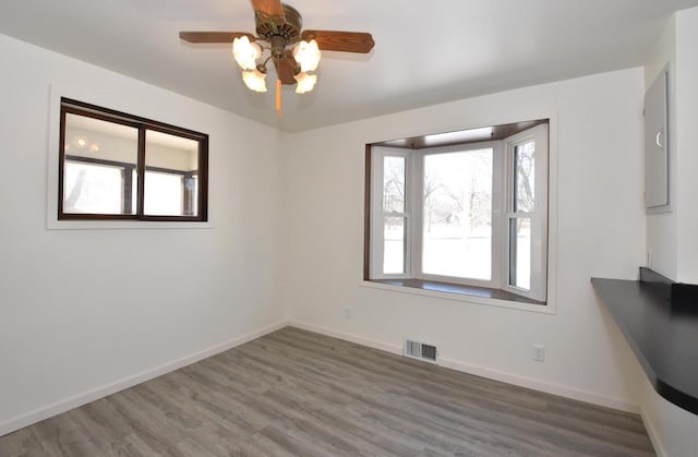 spare room featuring a ceiling fan, visible vents, baseboards, and wood finished floors