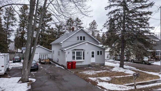 bungalow-style house with a garage, aphalt driveway, a chimney, and an outdoor structure