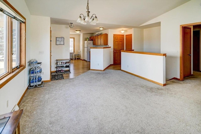 unfurnished living room featuring vaulted ceiling, a notable chandelier, light colored carpet, and baseboards