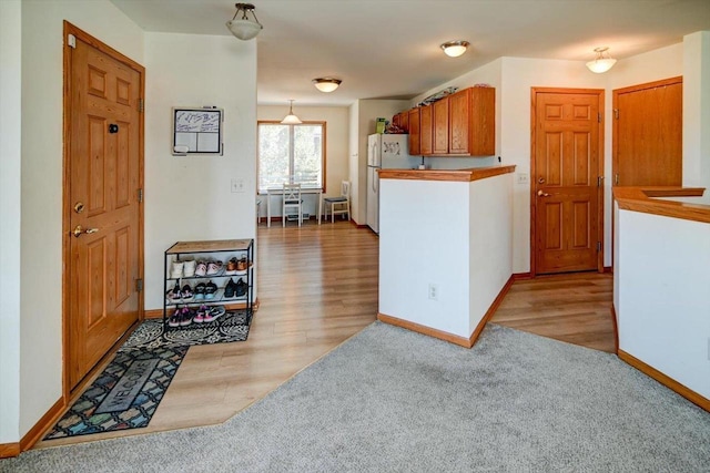 kitchen with light colored carpet, baseboards, freestanding refrigerator, and light wood-type flooring