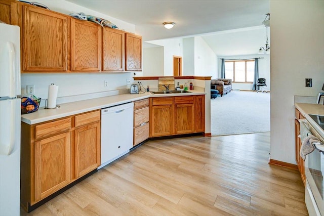 kitchen featuring light wood-style flooring, a sink, white appliances, a peninsula, and light countertops