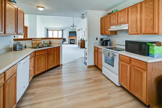 kitchen with under cabinet range hood, light wood-type flooring, a glass covered fireplace, white appliances, and a sink