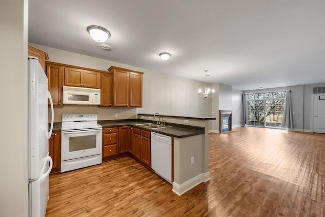 kitchen with a peninsula, white appliances, light wood-style floors, open floor plan, and brown cabinetry