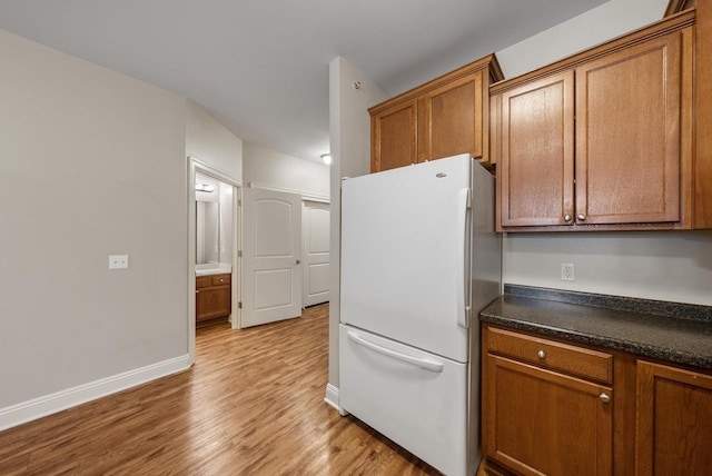 kitchen featuring dark countertops, light wood-style flooring, brown cabinetry, and freestanding refrigerator