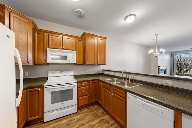 kitchen with white appliances, light wood finished floors, dark countertops, brown cabinets, and a sink