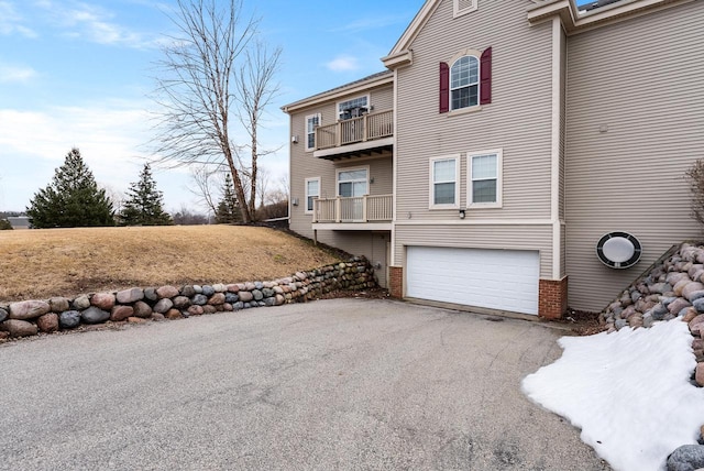 view of home's exterior featuring a balcony, an attached garage, aphalt driveway, and brick siding