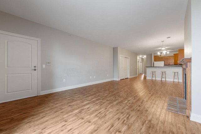 unfurnished living room with baseboards, light wood-style flooring, and a notable chandelier