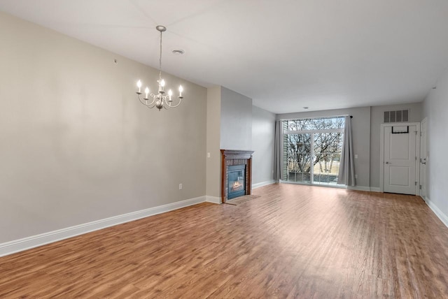 unfurnished living room with baseboards, visible vents, a fireplace with flush hearth, wood finished floors, and a chandelier