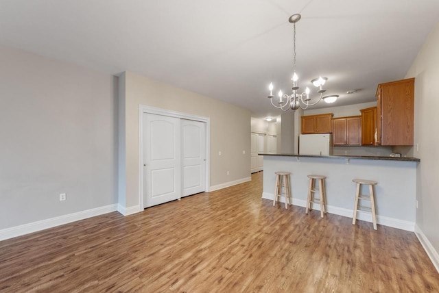 kitchen featuring a notable chandelier, light wood finished floors, dark countertops, brown cabinetry, and freestanding refrigerator