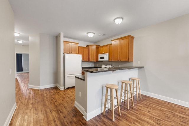 kitchen with a peninsula, white appliances, wood finished floors, baseboards, and a kitchen breakfast bar