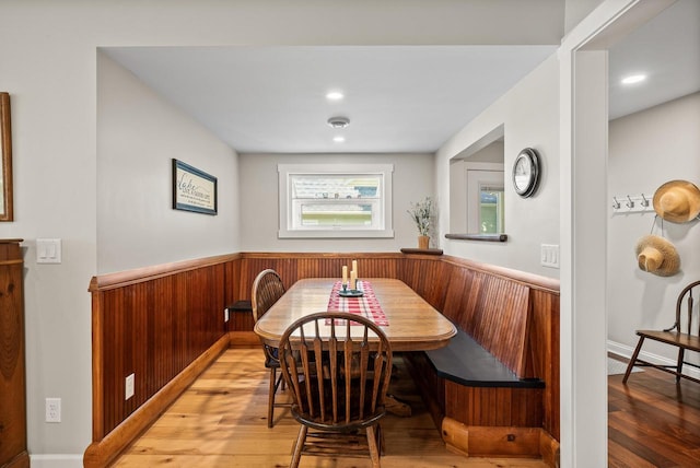 dining space featuring a wainscoted wall, light wood-style flooring, breakfast area, wood walls, and recessed lighting