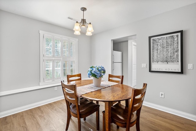 dining space featuring a chandelier, wood finished floors, visible vents, and baseboards