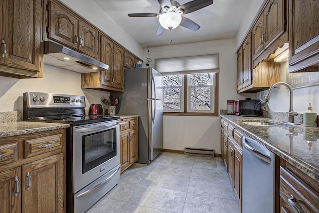 kitchen with baseboards, appliances with stainless steel finishes, stone counters, under cabinet range hood, and a sink